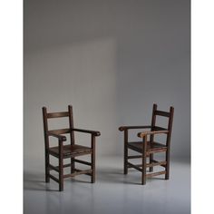 two wooden chairs sitting next to each other on a white floor in front of a wall