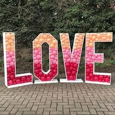 the letters love are made out of balloons and sit in front of a brick walkway