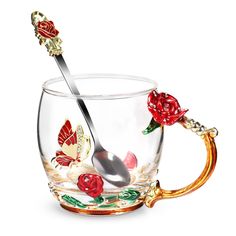 a glass cup with a spoon in it and some flowers on the inside, sitting next to a gold handle