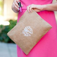 a woman in a pink dress holding a monogrammed clutch bag and writing on it