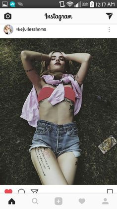 a woman laying in the grass with her arms behind her head and tattoos on her chest