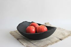 three apples in a black bowl sitting on a table cloth next to a white wall