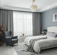 a bedroom with gray walls and white bedding, grey chair, and chandelier