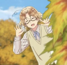 a person with glasses and a sweater on standing in front of some autumn leaves holding their hands up