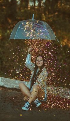 a woman sitting on the ground under an umbrella with confetti all around her