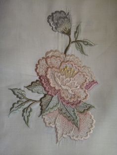 an embroidered piece of cloth with pink flowers on white fabric, including green leaves and stems