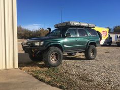 a green suv parked in front of a building with a trailer attached to it's roof