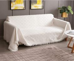 a couch covered in a white blanket next to a table with a potted plant