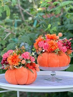 two pumpkin shaped vases filled with flowers sit on a white table in front of some bushes