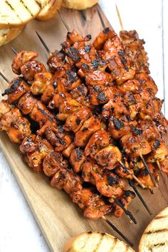 several skewers of chicken sitting on top of a cutting board next to bread