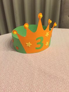 a green and orange crown sitting on top of a table next to a pink curtain