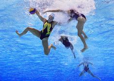 three people are swimming in the pool with water splashing on them and one is holding a ball