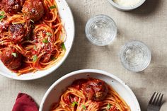 two bowls filled with spaghetti and meatballs on top of a table next to silverware