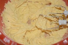 a red bowl filled with yellow batter and whisk attachments on top of it