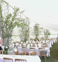 an outdoor tent with tables and chairs set up for a wedding reception in the grass