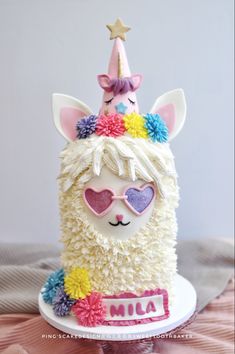 a birthday cake decorated with an alpaca wearing sunglasses and a unicorn horn hat