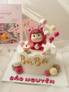 a birthday cake with a doll on top and balloons in the shape of hearts, sitting next to a card that reads happy birthday boi boi boi boi ney