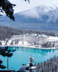 a large building sitting on top of a snow covered mountain next to a lake and forest