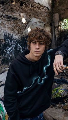 a young man standing in front of a graffiti covered wall with his hand on his hip