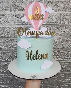 a blue cake with gold lettering and a hot air balloon on top that reads 9 meses tempeosa alelema