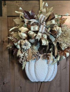 a white pumpkin hanging on a wooden door with fall foliage and flowers in the center