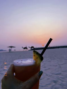 a person holding up a drink in front of the ocean at sunset or sunrise time