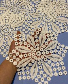 a hand is holding some white doily on a table