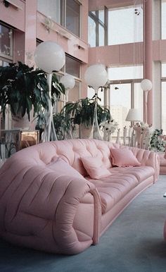 a living room filled with pink couches next to tall windows and potted plants