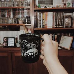 a person holding up a coffee cup in front of a book shelf filled with books