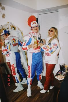 two women and one man are standing in front of a mirror wearing racing gear while drinking beer