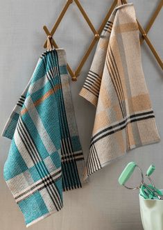 two teal and beige towels hanging on a rack next to a toothbrush holder