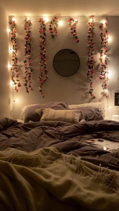 an unmade bed with lights hanging from the headboard and above it is a round mirror