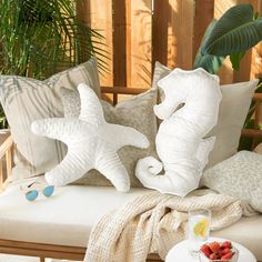 two white pillows sitting on top of a wooden bench next to a table with fruit