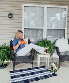 a woman sitting on a chair in front of a window holding a coffee cup and looking at the camera