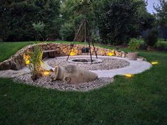 an outdoor fire pit surrounded by rocks and plants with lights on the ground around it