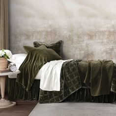 a bed with green bedspread and pillows in front of a gray painted wall