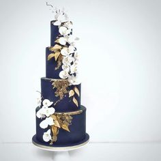 a three tiered blue cake with white and gold flowers on the top, sitting on a plate