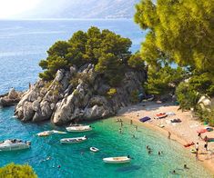 people are on the beach with boats in the water and trees around them, surrounded by rocks