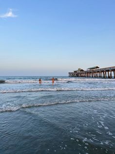 two people are swimming in the ocean near a pier