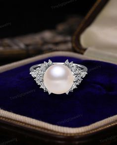 a white pearl and diamond ring in a velvet box with blue velvet lining the bottom