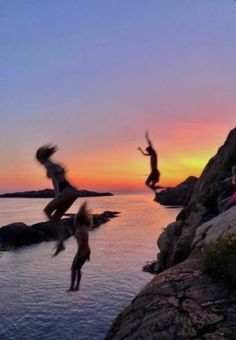 people jumping off rocks into the water at sunset