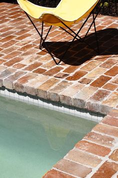 a yellow chair sitting on top of a brick patio next to a small swimming pool