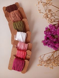 several spools of thread sitting on top of a piece of cardboard next to flowers