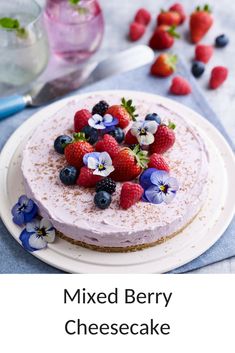 there is a cake with berries and blue flowers on the top, next to a glass of water