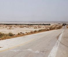 an empty road with no cars on it in the middle of nowhere, surrounded by desert