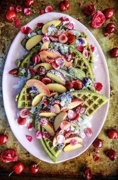 a white plate topped with waffles covered in fruit and powdered sugar next to cherries