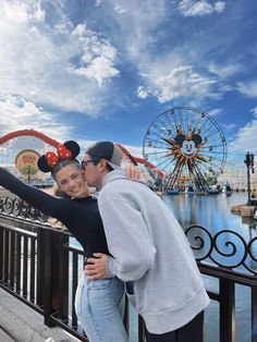 a man and woman standing next to each other in front of a ferris wheel at disney world