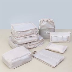 six pieces of white luggage sitting on top of a table next to a bag and pillow