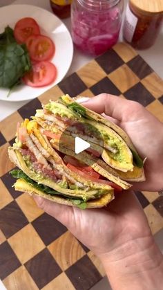 a person holding a sandwich in their hand on a checkerboard table with other food items