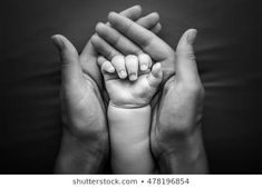 two hands holding a baby's hand in black and white, against a dark background